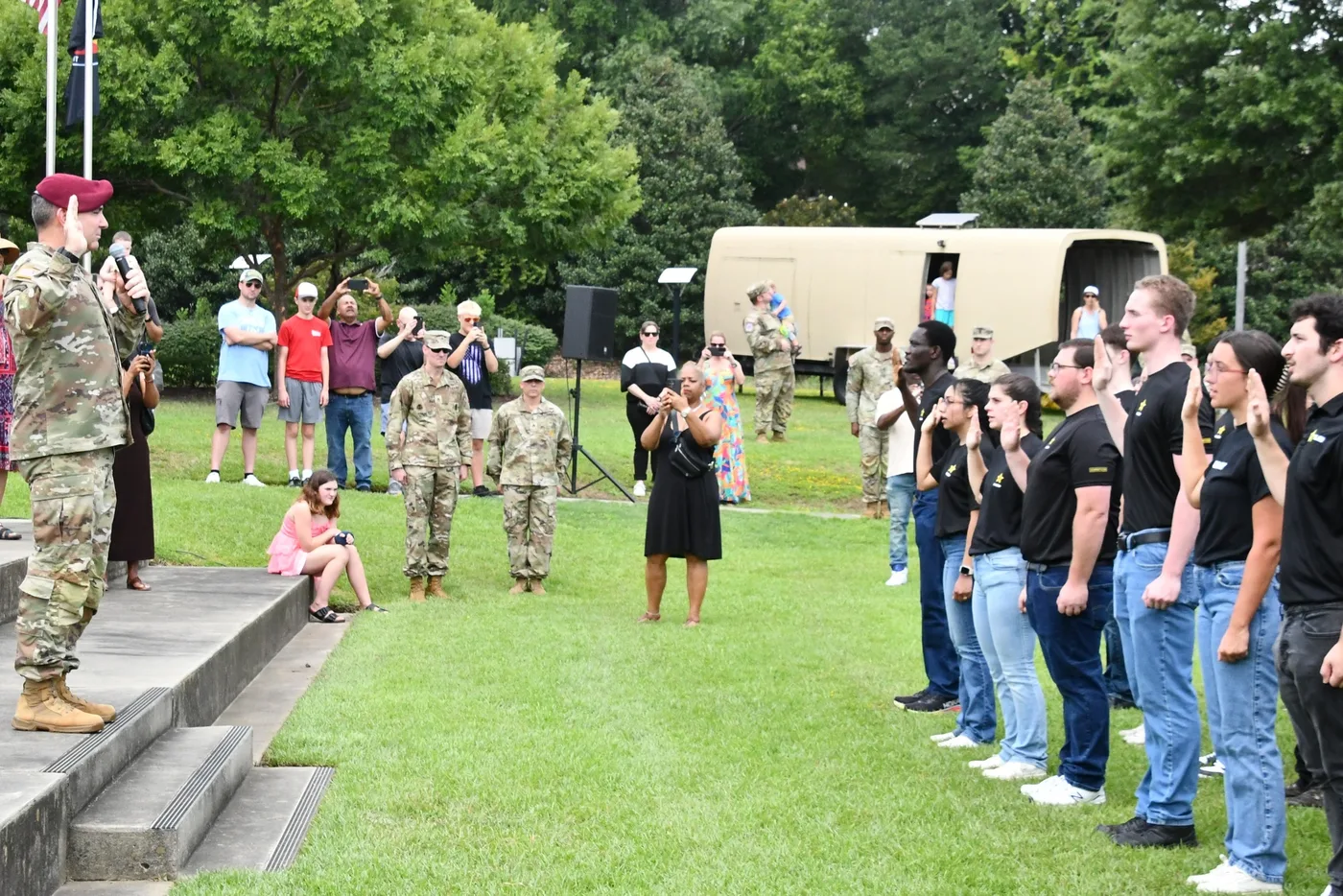 Army enlistees raise their right hands while a uniformed officer administers the oath outdoors
